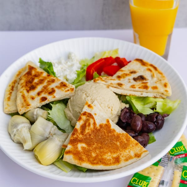 A Goldies Restaurant breakfast plate with hummus, pita bread, feta, olives, artichokes, and orange juice.