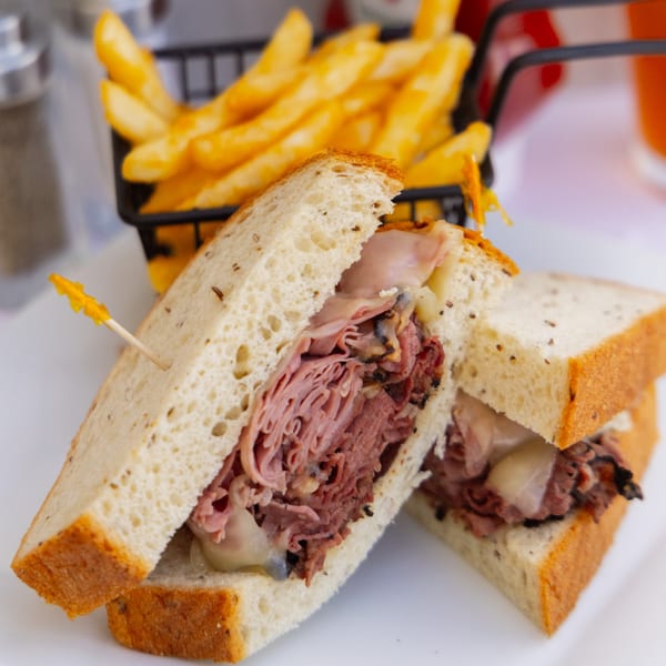 A Goldies Restaurant pastrami sandwich on rye with melted cheese and a side of golden fries.
