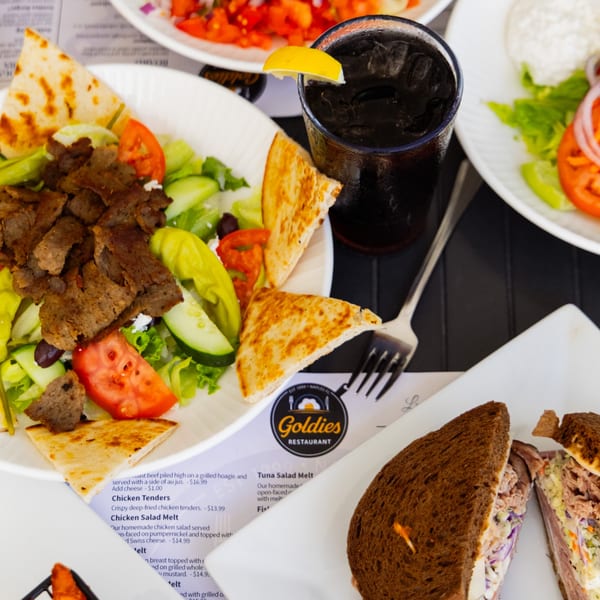 Goldies Restaurant breakfast spread with a gyro salad, tuna melt, and a drink with lemon.