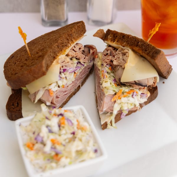 Goldies Restaurant's roast beef sandwich with coleslaw and cheese, cut in half, served with a side of coleslaw.