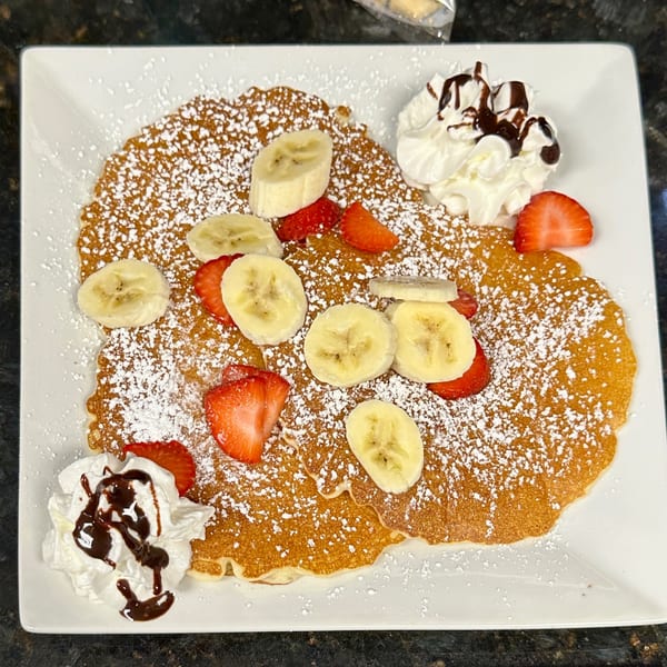 Goldies Restaurant pancakes with powdered sugar, sliced bananas, strawberries, whipped cream, and chocolate drizzle.